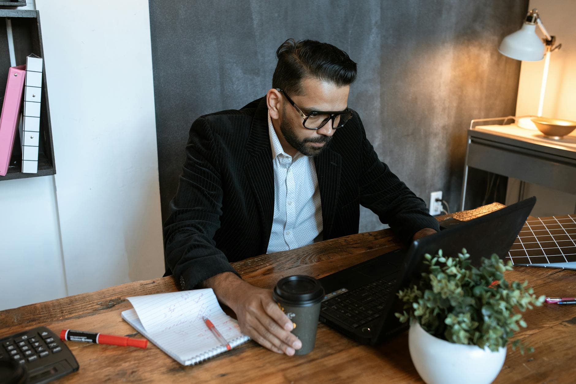 Man concentrating on laptop in a modern home office setting, coffee in hand.