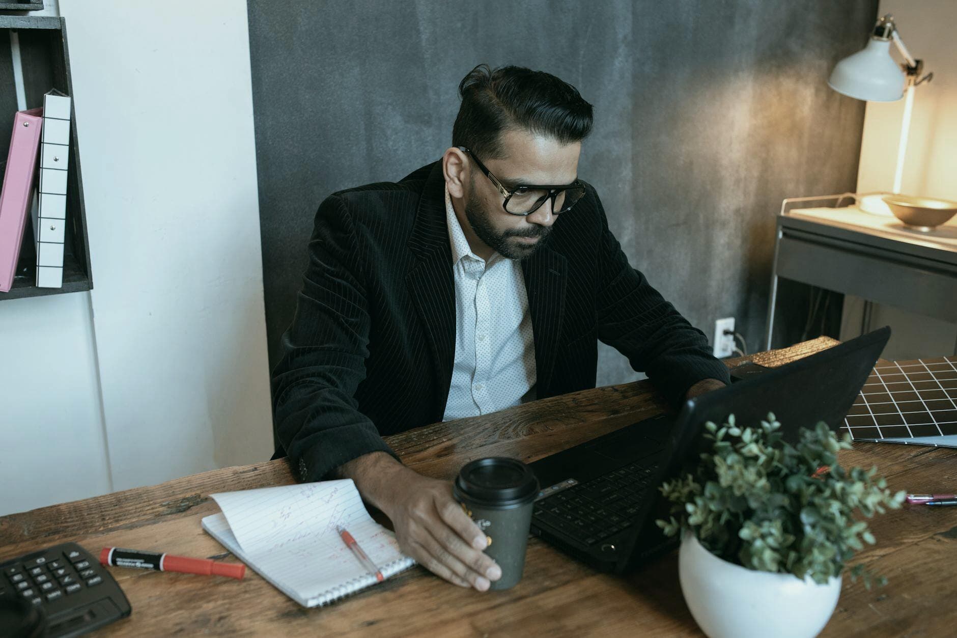 Man concentrating on laptop in a modern home office setting, coffee in hand.
