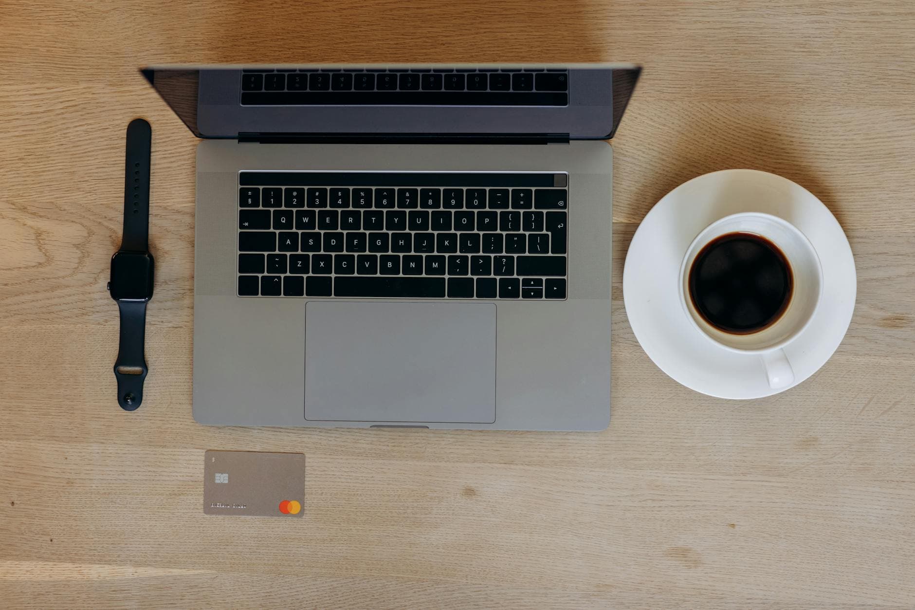 Flat lay of a laptop, smartwatch, credit card, and coffee on a wooden table. Perfect for tech-savvy professionals.
