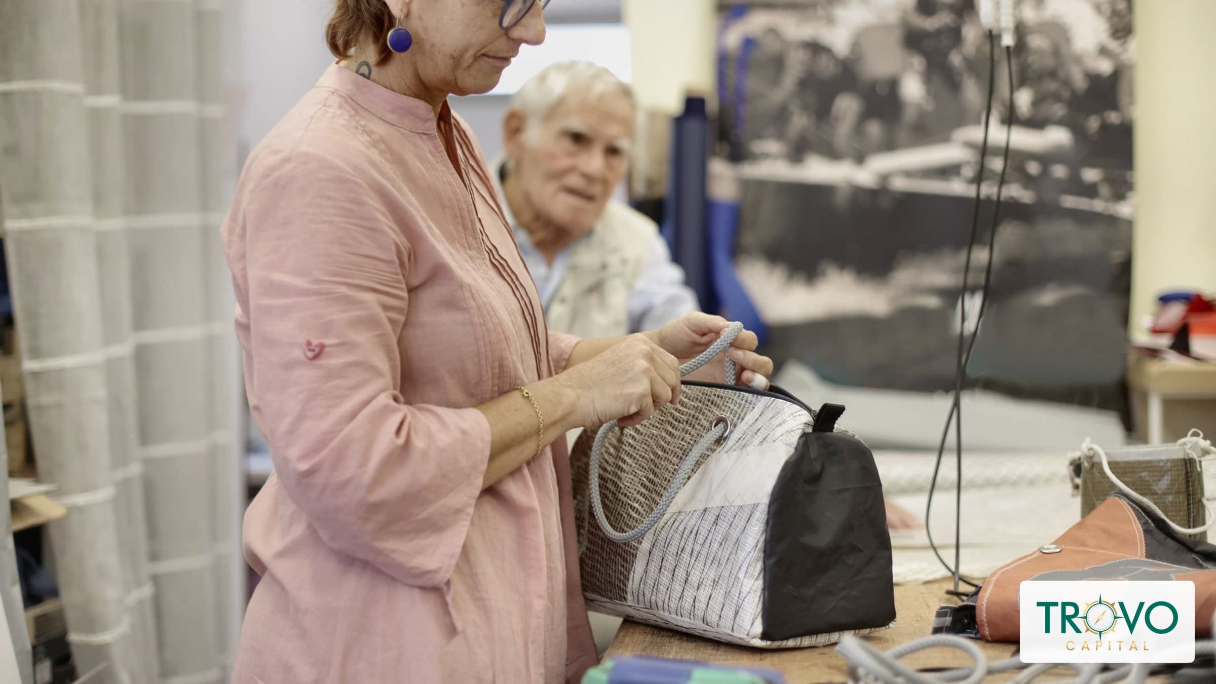A prospective customer tests a plain canvas bag while a maker observes in a small sewing studio.